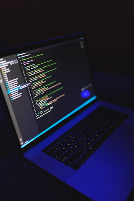 Close-up view of a smartphone screen displaying lines of computer code in various colors on a dark background, with the device tilted slightly to the right. The screen shows a programming interface, w